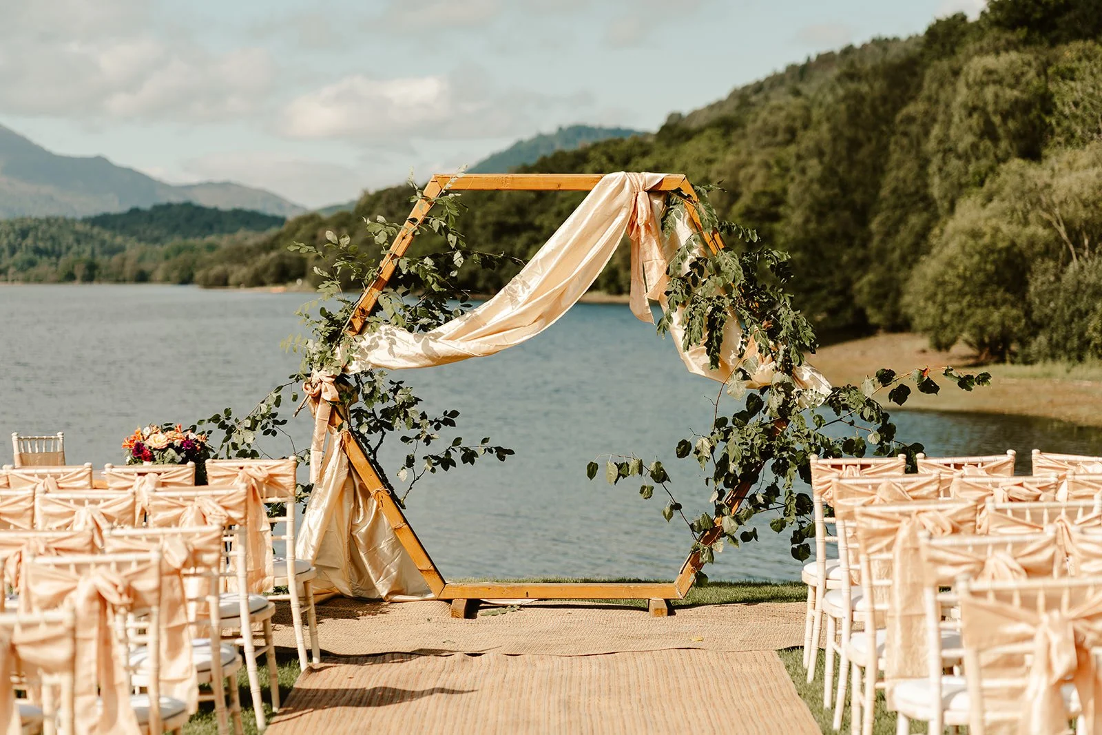 Hexagonal wedding arch draped with silk and foliage beside the loch