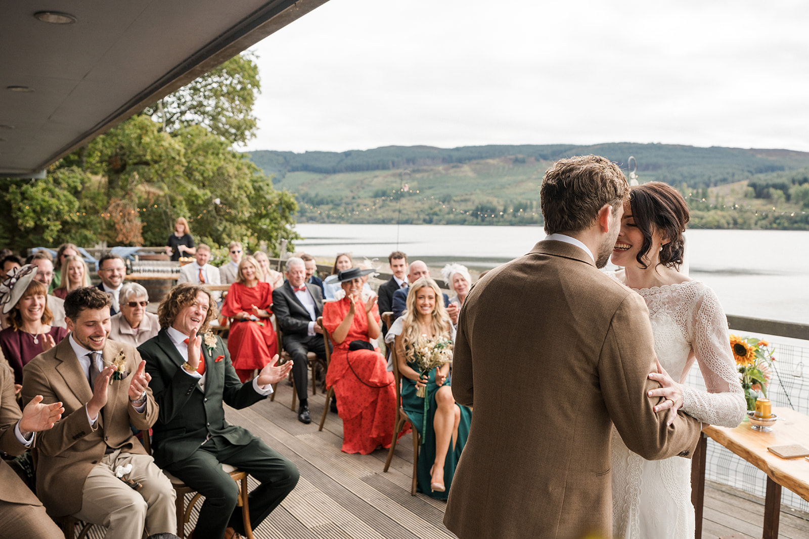 Newlyweds embrace on the deck as guests applaud