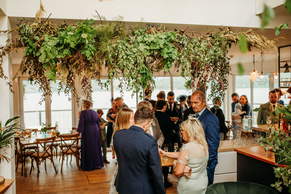Guests enjoying drinks beneath the foliage installation, loch beyond